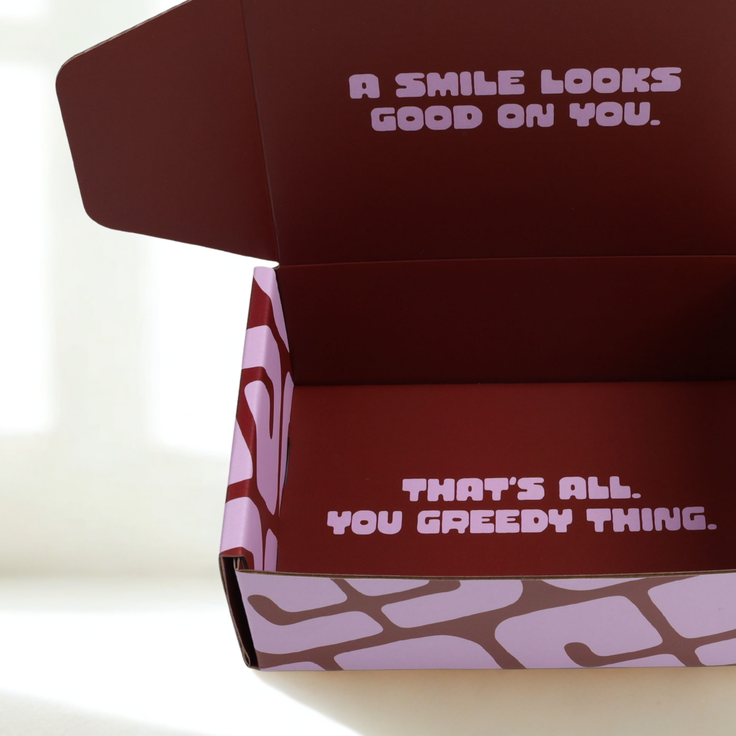 Boxwith text 'A smile looks good on you.' on lid and 'That's all. You greedy thing.' inside